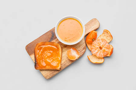 Board with bowl of tasty tangerine jam and toast on white backgroundの写真素材