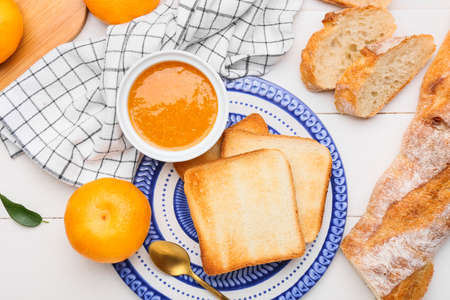 Bowl of tasty tangerine jam and bread on light wooden backgroundの写真素材