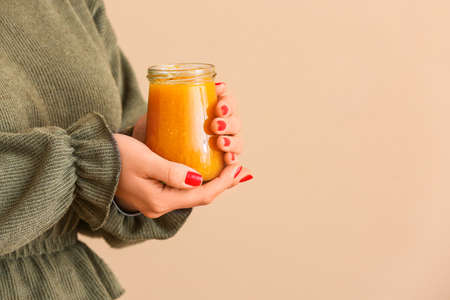Woman holding jar of tasty tangerine jam on color backgroundの写真素材