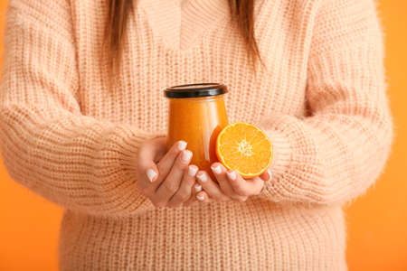 Woman holding jar of tasty tangerine jam on color backgroundの写真素材