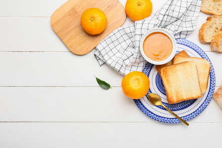 Composition with bowl of tasty tangerine jam and bread on light wooden background