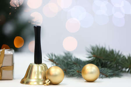 Golden Christmas bell and balls on table against blurred lights