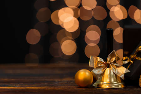 Christmas bell and toy on wooden table against blurred lights