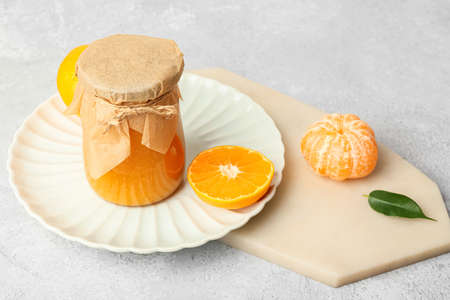Jar of tasty tangerine jam on light background