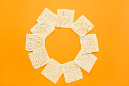 Frame made of Jewish flatbread matza for Passover on orange background