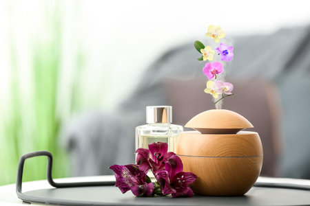 Aroma oil diffuser with flying orchid flowers on table in room