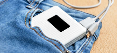 Modern power bank in pocket of jeans on beige background, closeupの写真素材