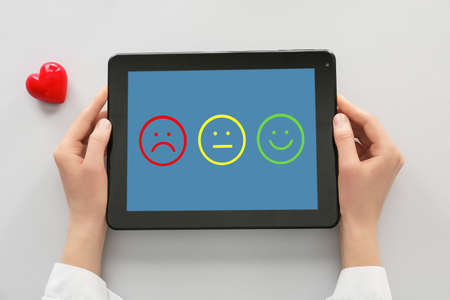 Female hands holding tablet computer with emoticons on screen against light background, top viewの写真素材