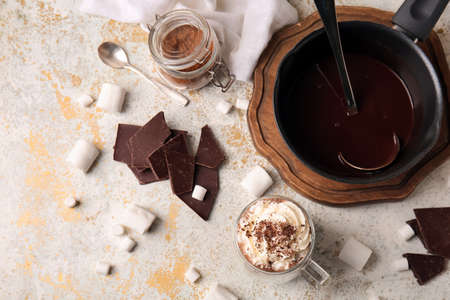 Glass cup of tasty hot chocolate and pot on light background