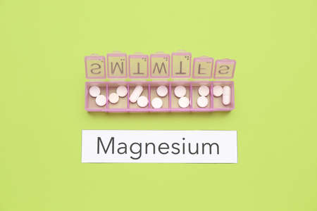 Plastic container with pills and word MAGNESIUM on green background