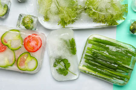 Fresh vegetables frozen in ice on color background