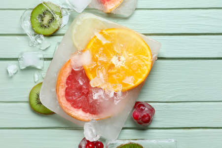 Fresh fruits frozen in ice on green wooden background