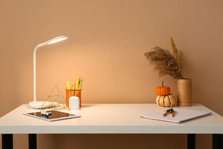 Tablet computer, earphones, notebook and glowing lamp on table near color wall