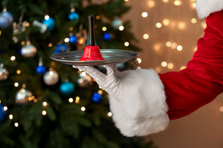 Santa Claus holding plate with Christmas bell against blurred fir tree