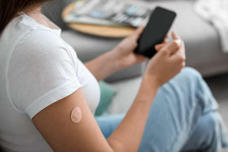 Young woman with applied nicotine patch using mobile phone at home. smoking cessationの写真素材
