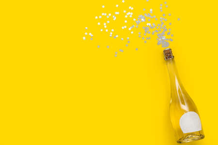 Bottle of champagne and beautiful confetti on yellow background