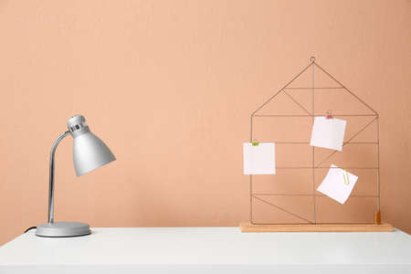 Modern lamp and board with sticky notes on table near color wallの写真素材