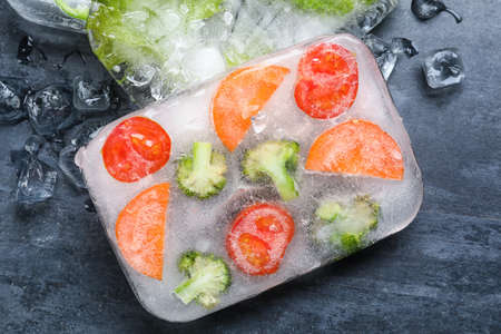 Fresh cut vegetables frozen in ice on dark background