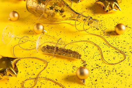 Champagne glass with confetti, bottle and Christmas decorations on yellow background