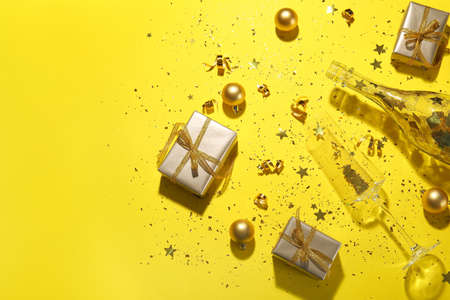 Composition with champagne glass, bottle, gift boxes and golden confetti on yellow backgroundの写真素材