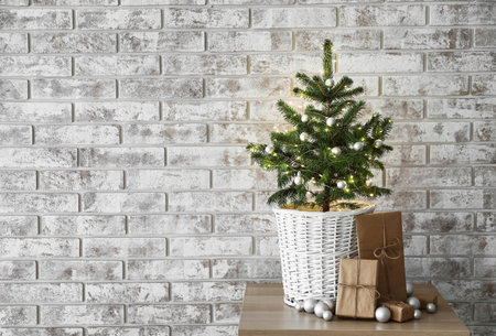 Beautiful decorated Christmas tree in pot and gift boxes near light brick wallの写真素材