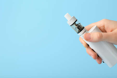 Female hand with modern vape mod on blue background, closeup