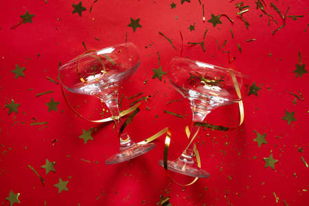 Champagne glasses, serpentine and golden confetti on red backgroundの写真素材