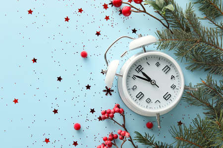 Stylish alarm clock, fir branches and berries on blue background