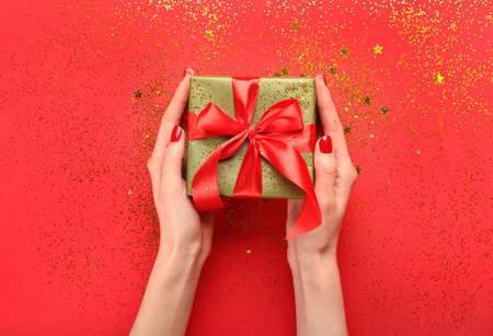 Female hands with Christmas gift and confetti on red backgroundの写真素材