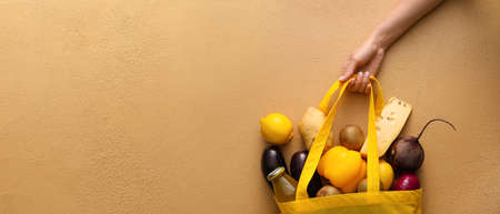 Hand and eco bag full of food on beige background with space for text