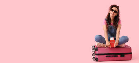 Young African-American woman with passport, tickets and suitcase on pink background with space for textの写真素材