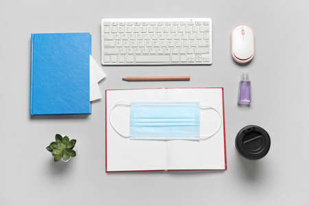 Notebooks, computer keyboard, mouse, medical mask and paper cup of coffee on gray backgroundの写真素材