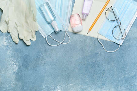 Medical masks, bottles with antiseptic, eyeglasses and stationery supplies on color backgroundの写真素材