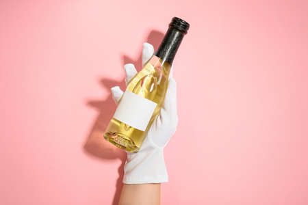 Female hand with bottle of champagne on pink backgroundの写真素材