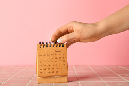 Female hand with craft calendar on pink backgroundの写真素材