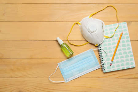 Notebook, pencil, medical masks and bottle with antiseptic on wooden backgroundの写真素材