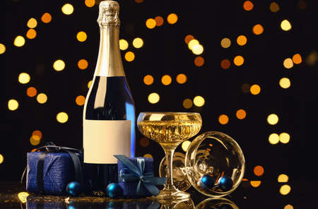 Bottle and glass of champagne with Christmas gift boxes on table against blurred backgroundの写真素材