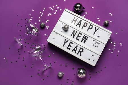 Board with text HAPPY NEW YEAR, champagne glasses and Christmas decor on purple backgroundの写真素材