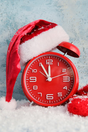 Stylish New Year clock, Santa hat and snow on blue background