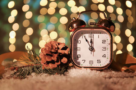Stylish New Year clock, Christmas decor and snow on table against blurred backgroundの写真素材