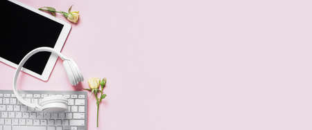 Tablet computer with headphones, keyboard and rose flowers on light pink background with space for...