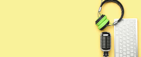 Headphones with microphone and computer keyboard on yellow background with space for text