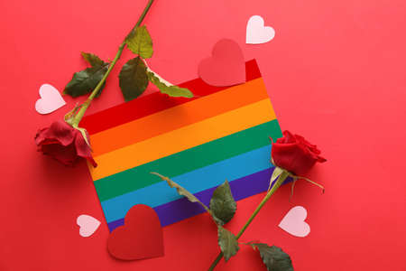 Composition with rainbow flag, rose flowers and paper hearts on red background. LGBT conceptの写真素材