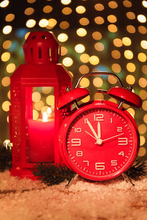 Stylish New Year clock, lantern and snow on table against blurred background