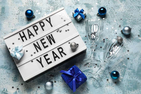 Board with text HAPPY NEW YEAR, glasses, gift boxes and Christmas decor on color backgroundの写真素材