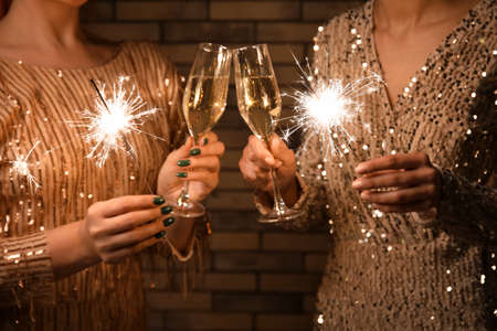 Young women with glasses of champagne and Christmas lights on brick wall background, closeupの写真素材