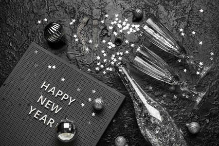 Board with text HAPPY NEW YEAR, glasses, opened champagne bottle and Christmas decor on black...