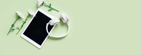 Tablet computer with headphones and flowers on green background with space for textの写真素材