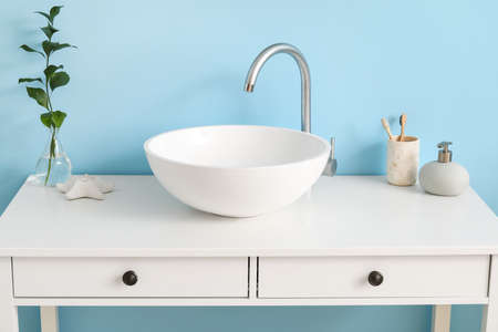 Table with sink, plant branch in vase and bath supplies near blue wall
