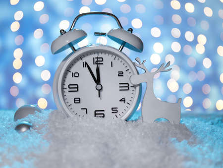 Stylish Christmas clock, decor and snow on table against blurred background